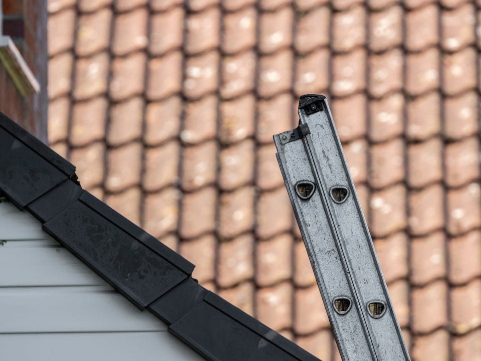 a metal extension ladder on a roof. Learn how to safely raise and lower an extension ladder with Matthews' Painting Company.