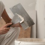 Woman taping and mudding joins pieces of drywall into a single solid wall. Fixing dry wall surface and preparation for painting.