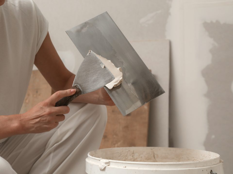Woman taping and mudding joins pieces of drywall into a single solid wall. Fixing dry wall surface and preparation for painting.