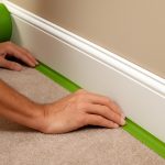 Applying green tape along baseboard to protect carpet. Matthews' Painting's professional painters expertly tape and protect your carpet.