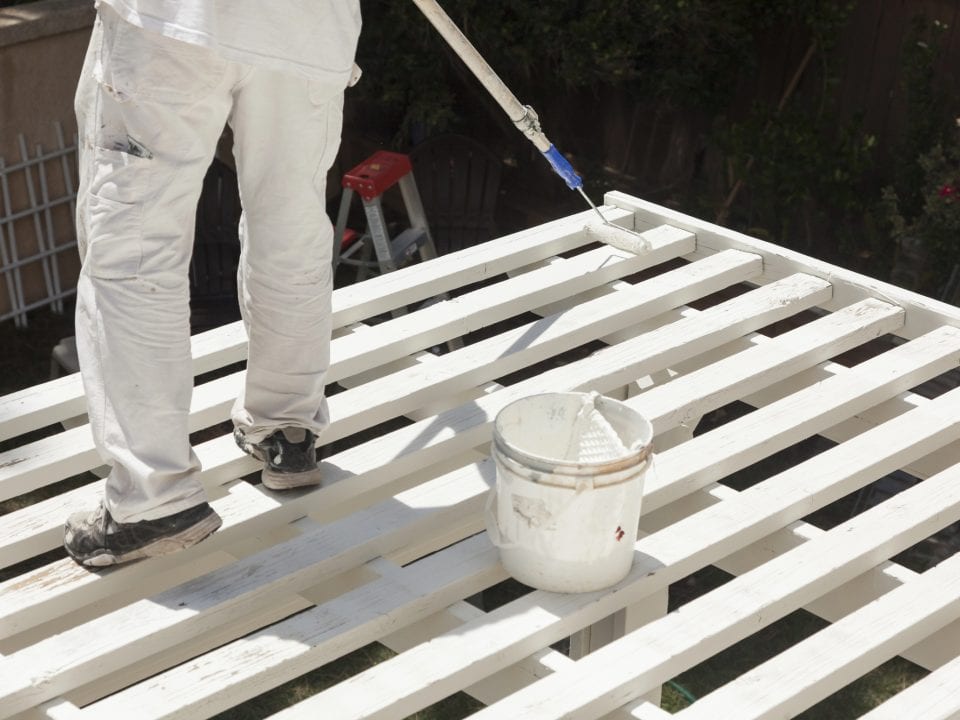 Painter Rolling White Paint Onto Top of Patio Cover
