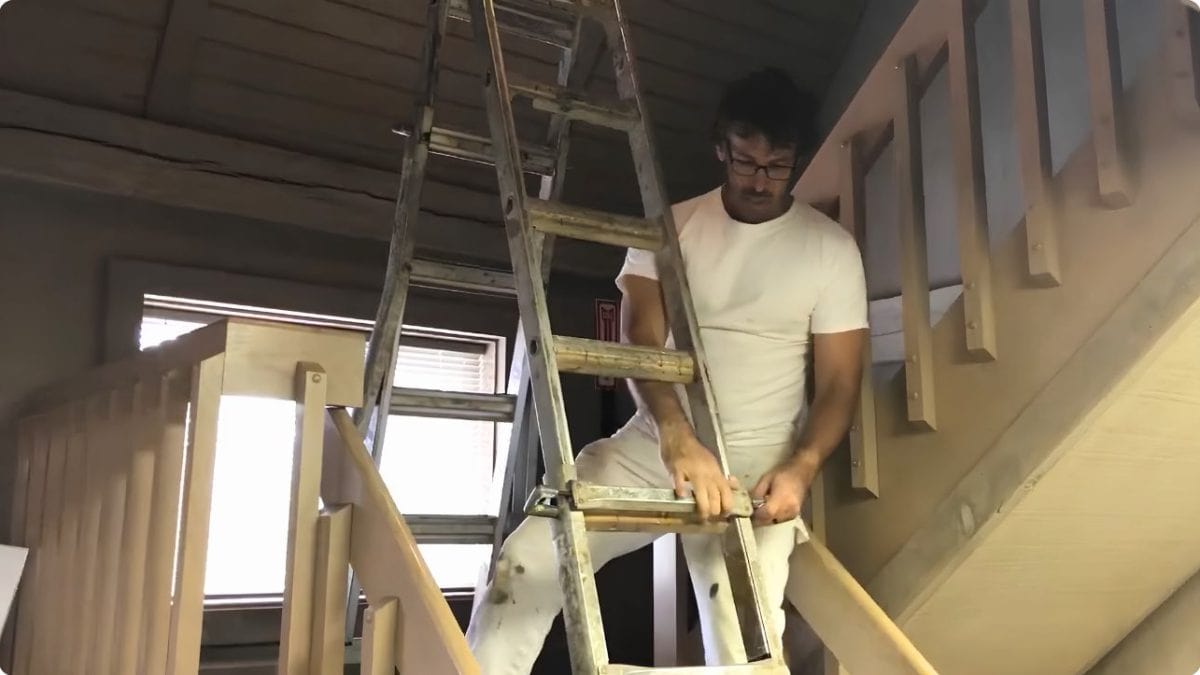 Professional painter safely setting up an adjustable ladder on a stairway for interior painting.