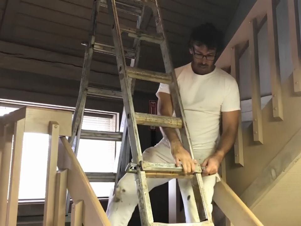 Professional painter safely setting up an adjustable ladder on a stairway for interior painting.